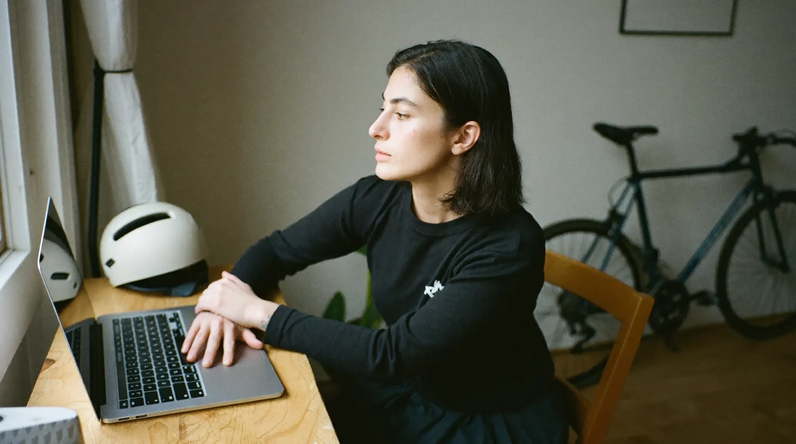 Cyclist sitting at a kitchen table at home, hand resting on a laptop, looking away from the screen and thinking