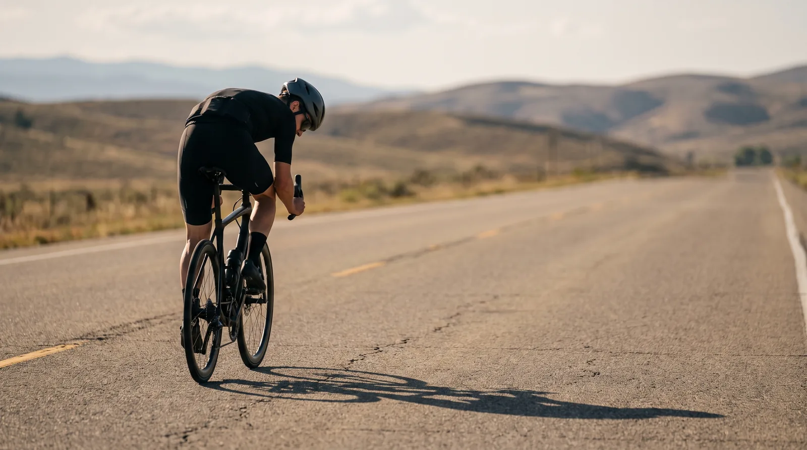 Lone cyclist deep into a long ride on an empty road, shoulders dropped, late afternoon light